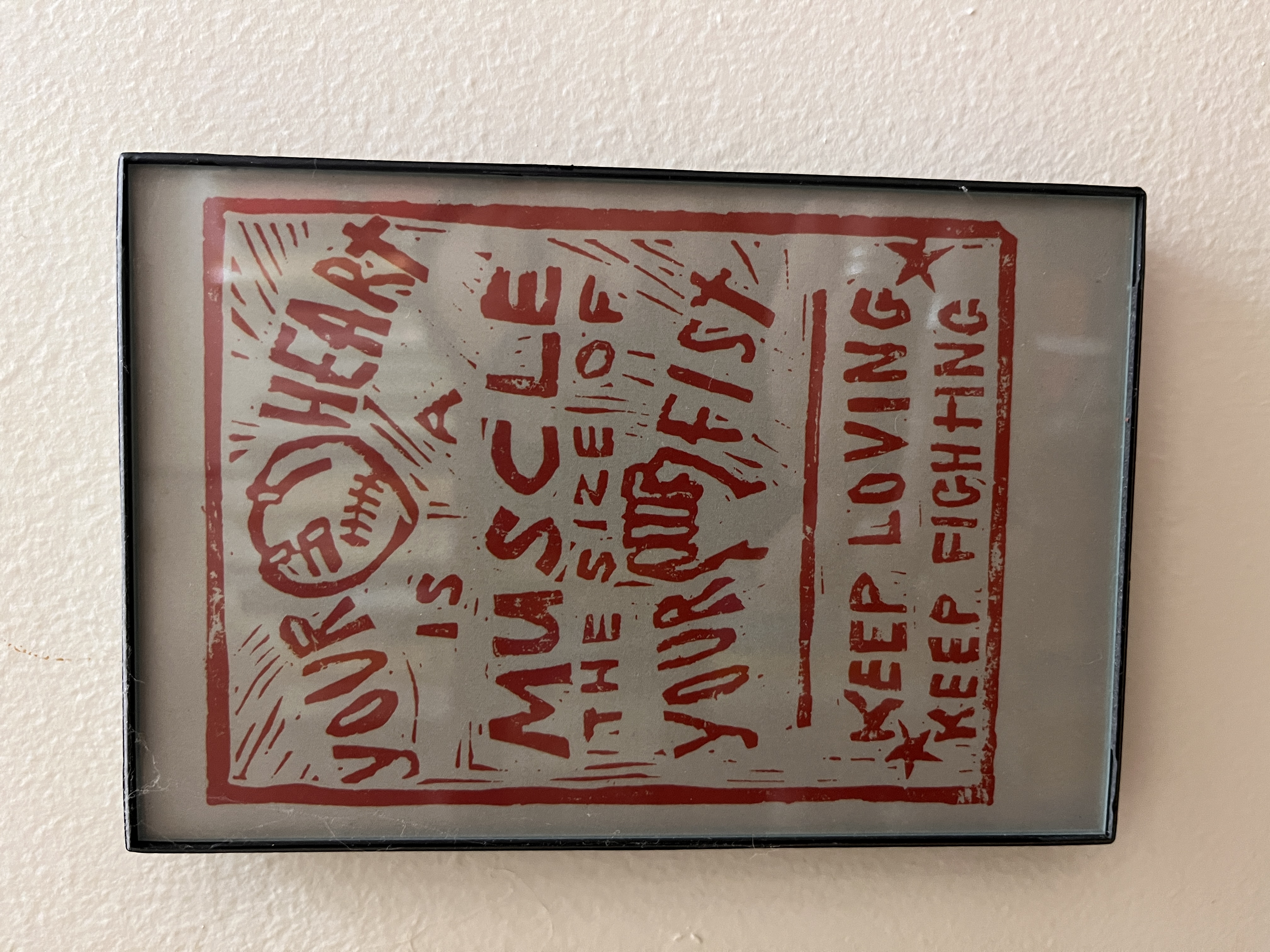 A red woodcut image with a fist and heart and the slogan "your heart is a muscle the size of your fist; keep loving; keep fighting."