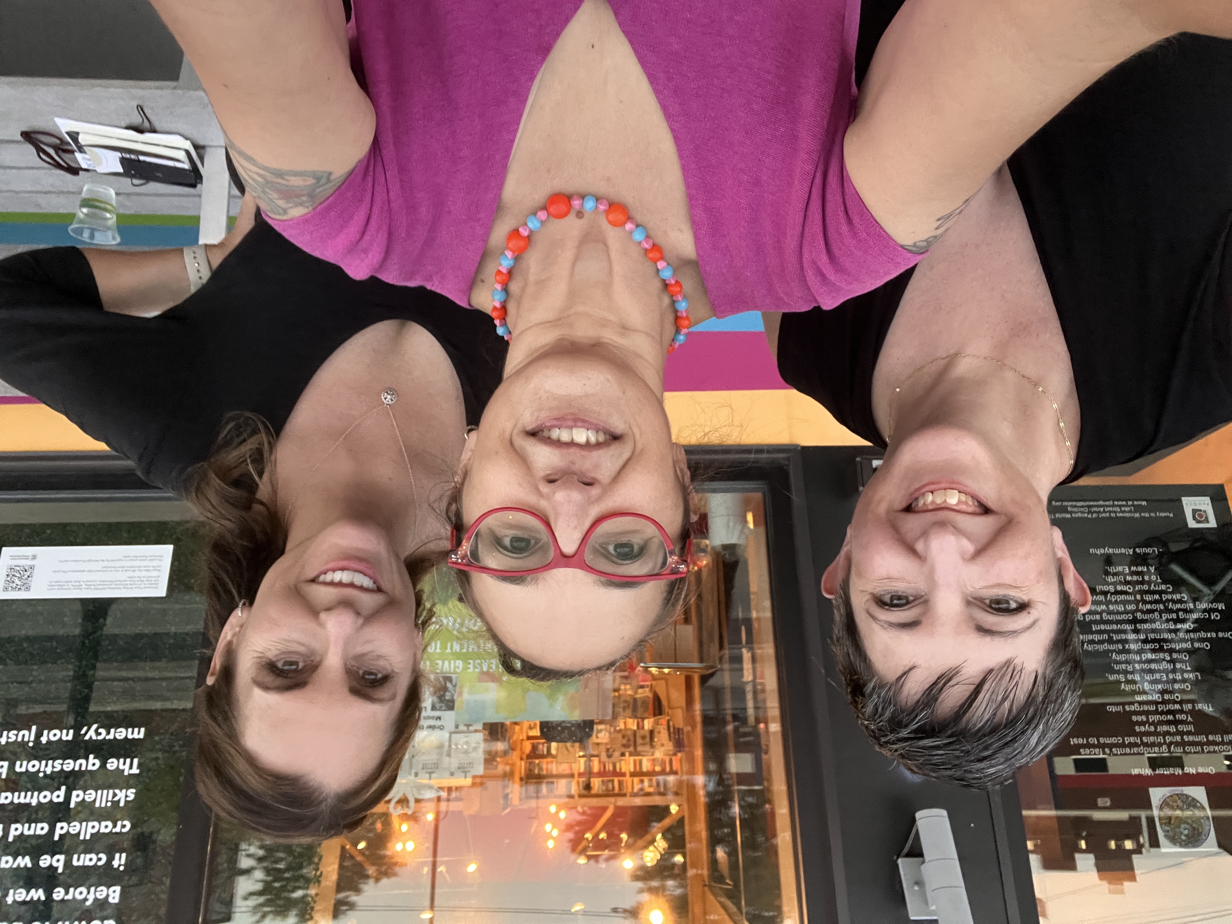 Heidi, Sonya, and Jeannine, three white women, one with red glasses, in front of a storefront with lights glowing inside and bookshelves.