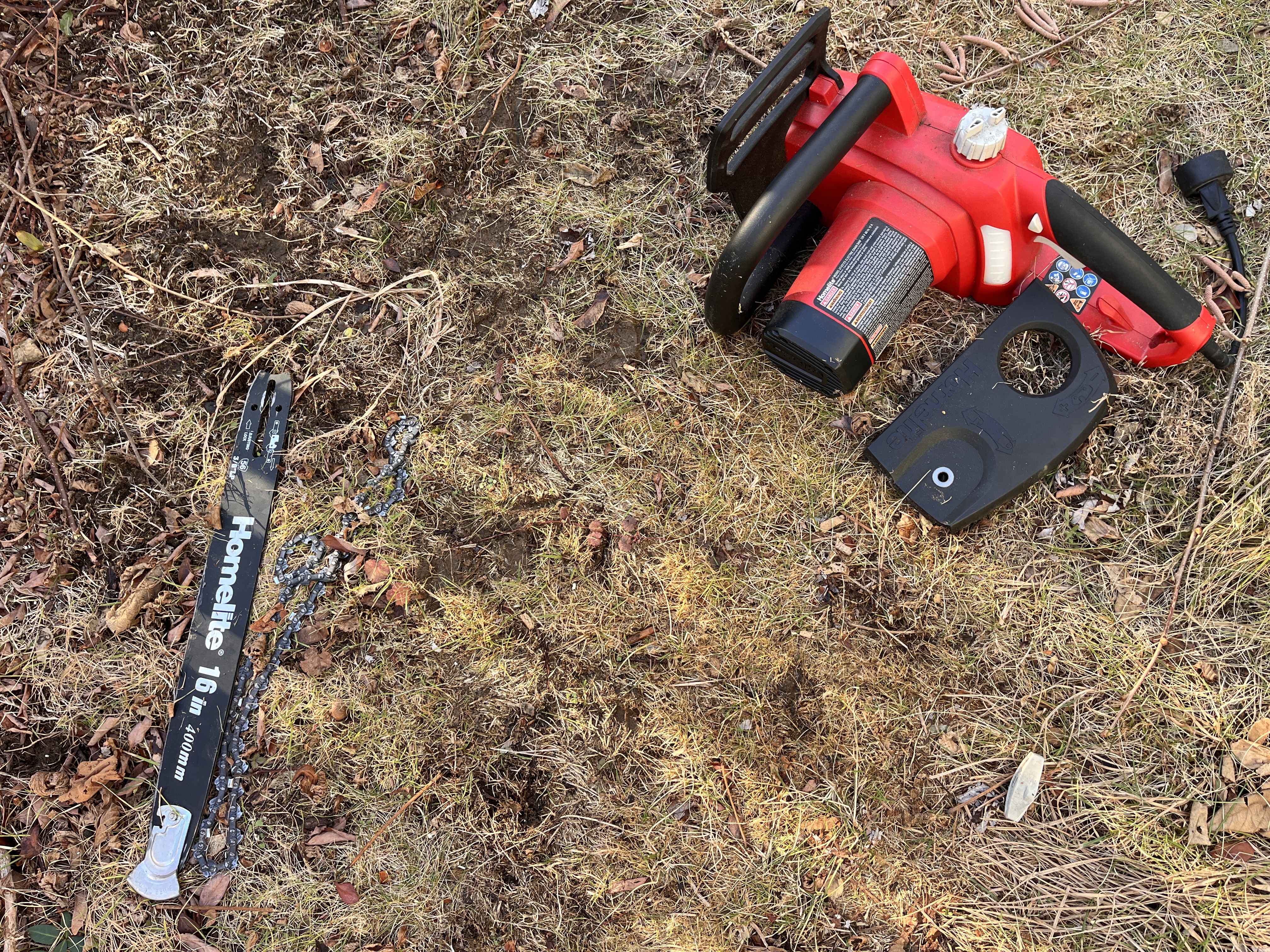 Pieces of a disassembled chainsaw with a red body on the brown lawn