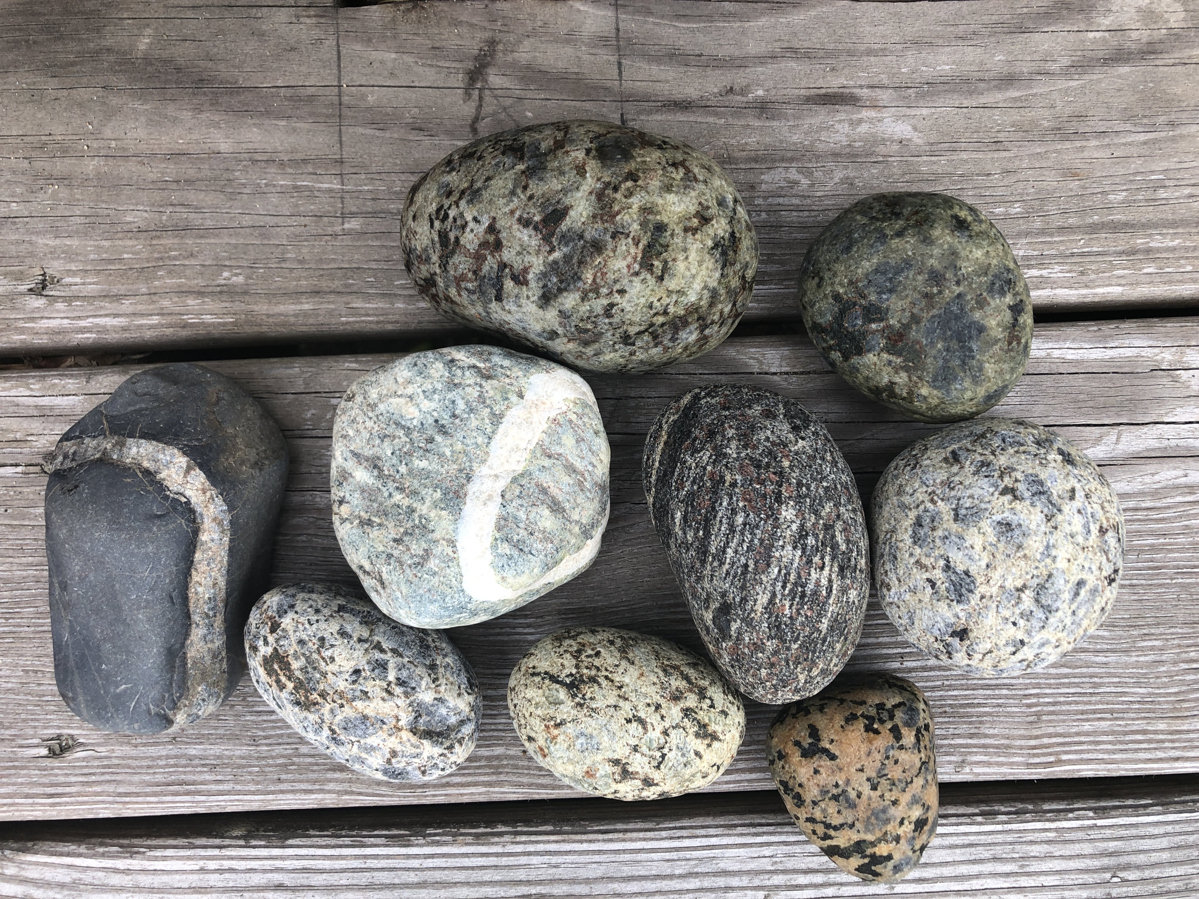 Seven stones on a worn picnic table, many of them with circles through them, most likely granite.