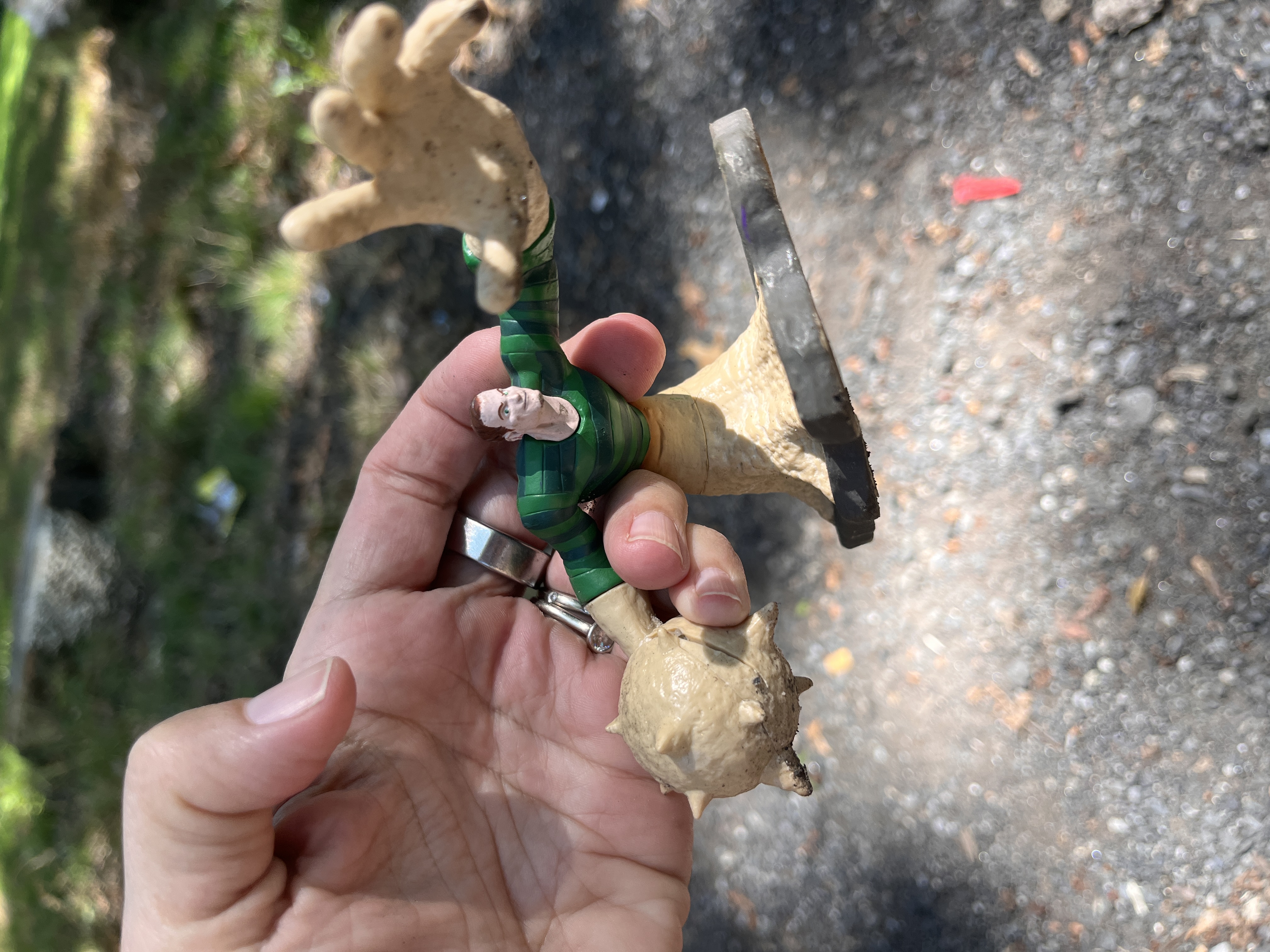 My hand holding an action figure of a white superhero man who has one hand reaching toward the viewer with the other hand turned into a spiky mace